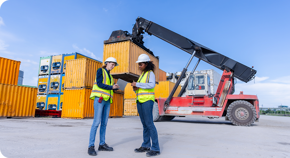 Vista de dos personas. Atrás se ve una grúa de carga, llevando contenedores. Al fondo se ven más contenedores.