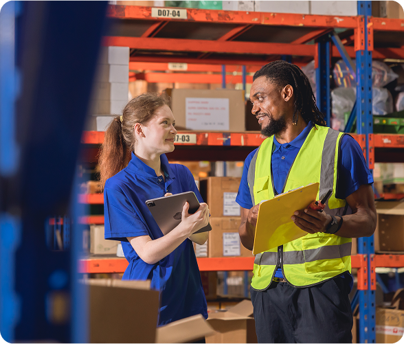 Vista de dos personas hablando en una bodega. Al fondo se ven cajas.