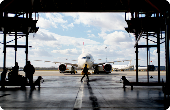 Vista frontal de un avión en una pista de despegue, al frente se ve una persona caminando y al lado izquierdo se ven las siluetas de dos personas.